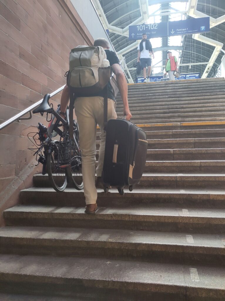 In der einen Hand das Faltrad, in der anderen der Koffer. Michael muss bei seiner Reise mit dem Zug sein Gepäck oft tragen.